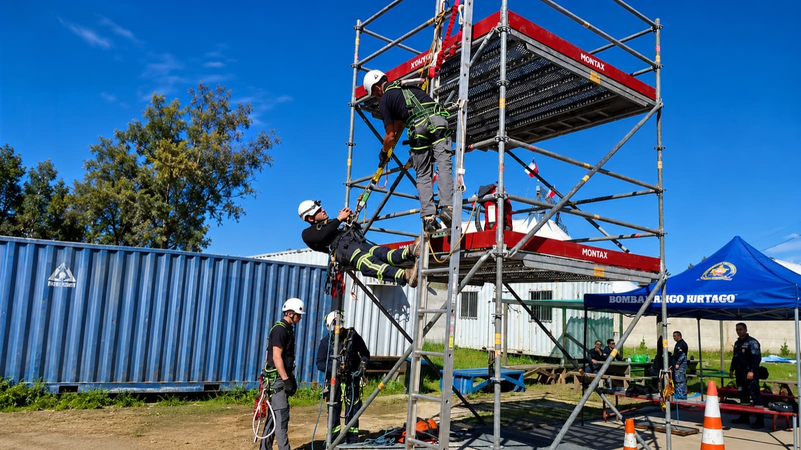 Instructores con arnés y sistemas de cuerda realizan una práctica de trabajo en altura y rescate sobre una torre de andamios.